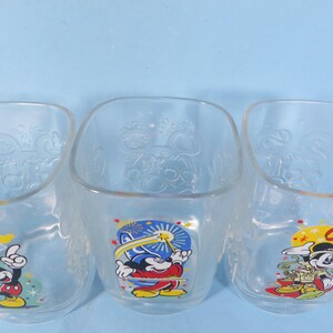 May include: Three clear, square-shaped glass bowls with Mickey Mouse graphics. Each bowl features a different pose of Mickey Mouse in colorful attire. The bowls have embossed designs and are set against a light blue background.