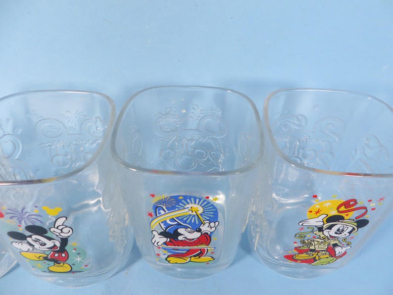 May include: Three clear, square-shaped glass bowls with Mickey Mouse graphics. Each bowl features a different pose of Mickey Mouse in colorful attire. The bowls have embossed designs and are set against a light blue background.