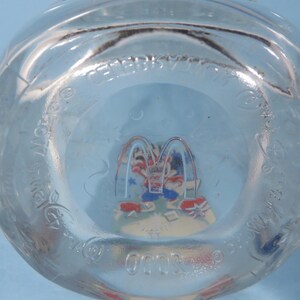 May include: Clear glass McDonald's cup with a colorful graphic of Ronald McDonald and friends. The cup has the McDonald's logo and text around the rim. The bottom of the cup features a colorful image of the McDonald's characters.
