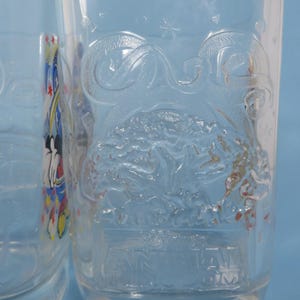 May include: Two clear glass tumblers with embossed designs. One features a stylized tree and the text "Walt Disney World". The other has a Mickey Mouse design. The glasses are on a light blue background.