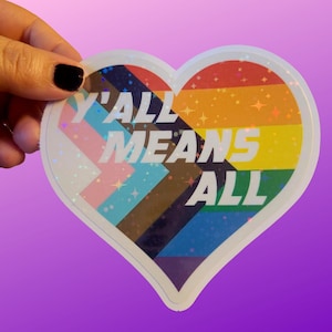 Op de afbeelding: Een hartvormige sticker met een regenboog-pride-vlagontwerp en de tekst "Y'all Means All" in witte letters.