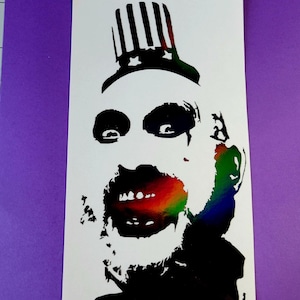 May include: A black and white silhouette of a person with a rainbow mouth and a hat with stars and stripes. The person is wearing a black shirt and has a beard.