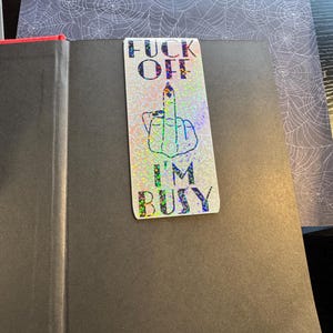 May include: A black and white sticker with a middle finger and the text "F**k Off I'm Busy" on a glittery background.