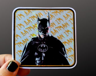Peut inclure: Un autocollant carré représentant Batman dans un graphisme noir et gris. L'autocollant a une bordure dorée et un fond avec les mots "I'M BATMAN" répétés. Le logo Batman est visible sur la poitrine.