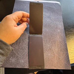 May include: A black, rectangular, foldable photo album with a spiderweb pattern on the cover.