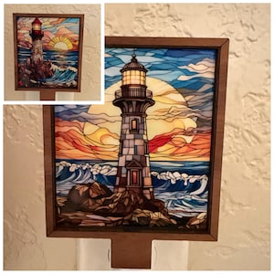 May include: A decorative night light featuring a stained-glass style image of a lighthouse. The lighthouse is gray and white, with a bright yellow light. The background shows a sunset over the ocean with blue waves and orange and yellow skies. The night light is framed in a brown wooden border.