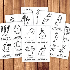 May include: Black and white printable flashcards featuring illustrations of various vegetables and fruits with cute faces. The cards include asparagus, potato, pumpkin, red pepper, cucumber, onion, carrot, zucchini, chili, corn, mushroom and cabbage.