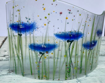 May include: A clear glass vase with a curved shape features a design of blue flowers with green stems and yellow, green, and pink dots.