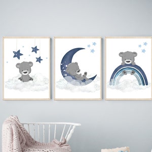 Op de afbeelding: Drie blauwe en grijze kinderkamerprints met een schattige beer op een halve maan, een beer op een regenboog en een beer met sterren die erboven hangen.