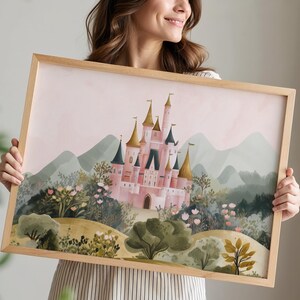 May include: A framed watercolor print of a pink castle with gold turrets, set against a backdrop of green hills and a soft pink sky. The artwork is in a light wooden frame.