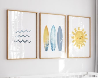 Puede incluir: Una cuna blanca con una manta beige, una almohada blanca con rayas negras y una almohada blanca con patrones geométricos en blanco y negro. Hay tres impresiones enmarcadas en la pared sobre la cuna. Las impresiones presentan un diseño de ola azul, un diseño de tabla de surf amarillo, azul y blanco, y un sol amarillo con una cara sonriente.