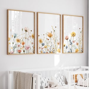 May include: Three framed watercolor paintings of colorful wildflowers on a white wall above a white crib with a white blanket and pillows.
