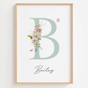 Puede incluir: Impresión enmarcada con una letra "B" verde claro adornada con flores y mariposas de acuarela. El nombre "Bailey" está escrito en cursiva debajo. La obra de arte se presenta sobre un fondo blanco, en un marco de madera.