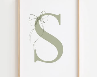 May include: A framed print featuring the letter "S" in a soft sage green color. A delicate bow design is artfully placed above the letter, with flowing lines adding an elegant touch. The artwork is set against a white background.