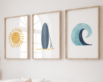 May include: Three framed illustrations of a sun, a surfboard, and a wave in a minimalist style. The illustrations are in shades of blue, yellow, and white. The frames are light wood.