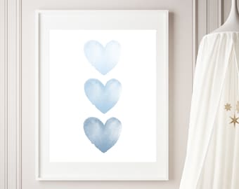 May include: A framed print featuring three watercolor hearts in varying shades of blue. The artwork is displayed in a white frame against a white wall. The room also includes a woven basket, a canopy, and decorative stars.