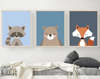 May include: Three framed prints with illustrations of a raccoon, a bear, and a fox. Each animal is depicted with closed eyes and a simple, cartoon-like style. The prints are set against a light blue, blue, and dark blue background, respectively.