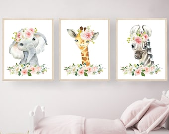 May include: Three framed watercolor paintings of animals with floral crowns. The animals are an elephant, a giraffe, and a zebra. The paintings are on a white background and have a light wood frame.