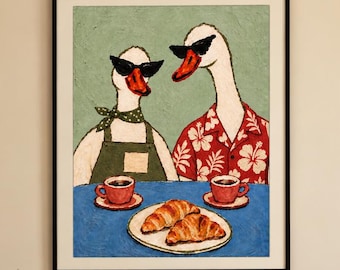 May include: A framed wall art print featuring two white geese wearing black sunglasses. One goose wears a green apron and neckerchief, while the other wears a red floral shirt. They sit at a blue table with two red coffee cups and a plate of croissants.
