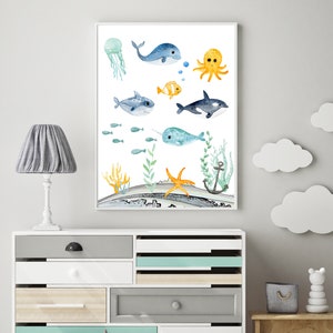 Peut inclure: Une illustration aquarelle d'une vari&eacute;t&eacute; de cr&eacute;atures marines, dont une baleine, une pieuvre, une narval, un requin, une m&eacute;duse et une &eacute;toile de mer. L'illustration est sur un fond blanc avec un motif de vague bleu et gris en bas.
