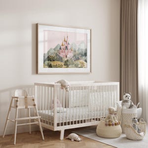 May include: A framed watercolor print of a pink castle with gold turrets, set against a backdrop of green hills and a pink sky. A white crib, high chair, and baskets filled with stuffed animals complete the nursery decor.