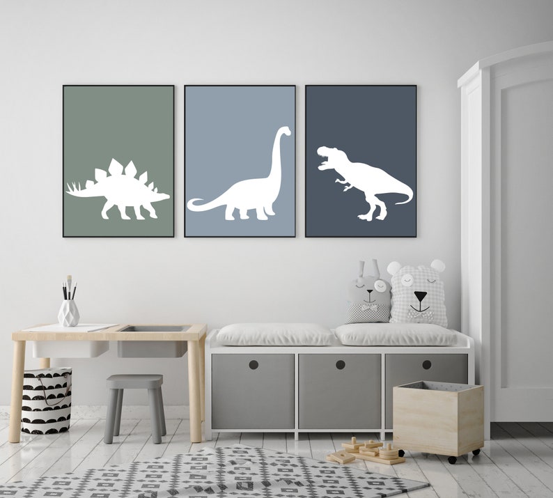 May include: Three framed prints of white dinosaur silhouettes on a blue and green background. The prints are hanging on a white wall above a white bench with storage bins and a wooden toy bin.