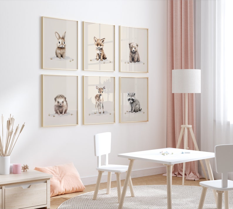 May include: A set of six framed animal prints featuring a rabbit, fox, bear, hedgehog, deer, and raccoon. The prints are in a minimalist style with a white background and gold frames. The prints are hung on a white wall with a pink curtain in the background.