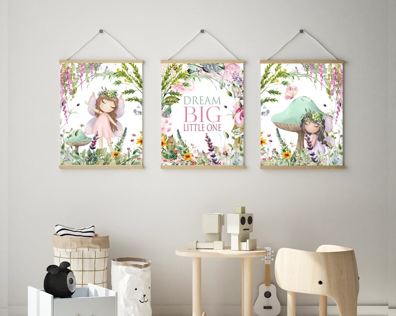 May include: Three framed prints with a whimsical fairy theme. The center print features the text "Dream Big Little One" surrounded by flowers and greenery. The left print shows a fairy with pink wings and a pink dress standing in a forest setting. The right print shows a fairy sitting on a mushroom with a butterfly flying above.