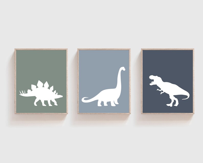 May include: Three framed prints with white dinosaur silhouettes on different colored backgrounds. The left print has a green background and a stegosaurus silhouette. The middle print has a light blue background and a brachiosaurus silhouette. The right print has a dark blue background and a tyrannosaurus rex silhouette.