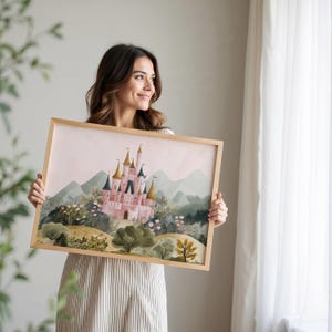 May include: A framed watercolor print of a pink castle with gold turrets, set against a backdrop of green hills and a soft pink sky. The artwork is in a light wood frame, showcasing a fairytale landscape.