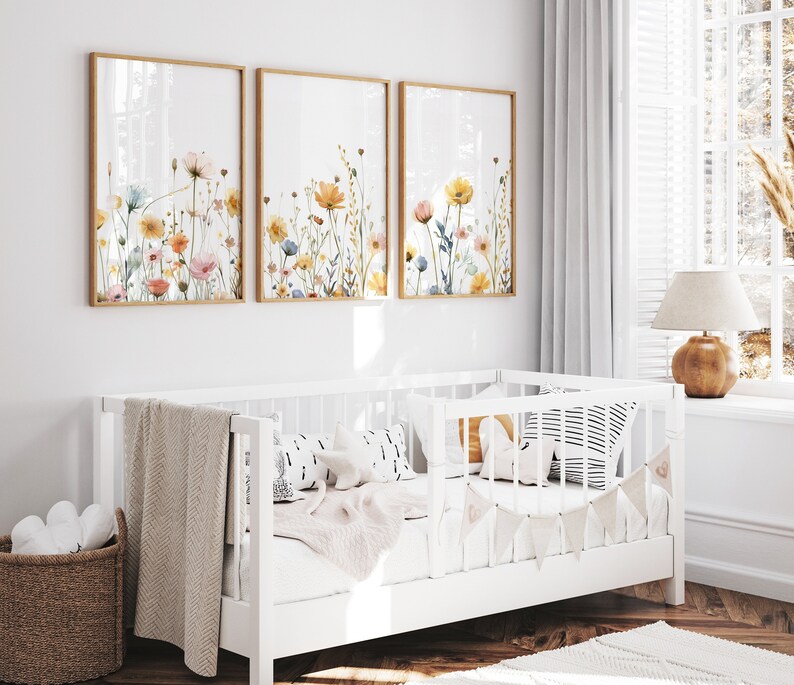 May include: Three framed watercolor paintings of colorful wildflowers on a white wall above a white crib with a white blanket and pillows.