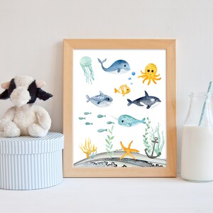 Peut inclure: Une illustration aquarelle de diff&eacute;rentes cr&eacute;atures marines, dont une baleine, une pieuvre, un requin, une narval et des poissons. L'illustration est sur un fond blanc avec des algues bleues et vertes et une &eacute;toile de mer jaune.