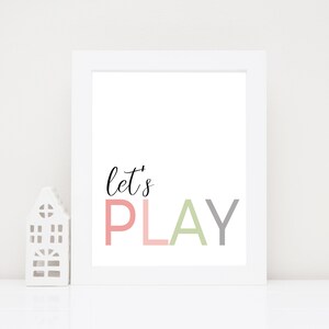 May include: White framed print with the text "let's PLAY" in pink, green, and gray letters. The letters are stacked on top of each other.