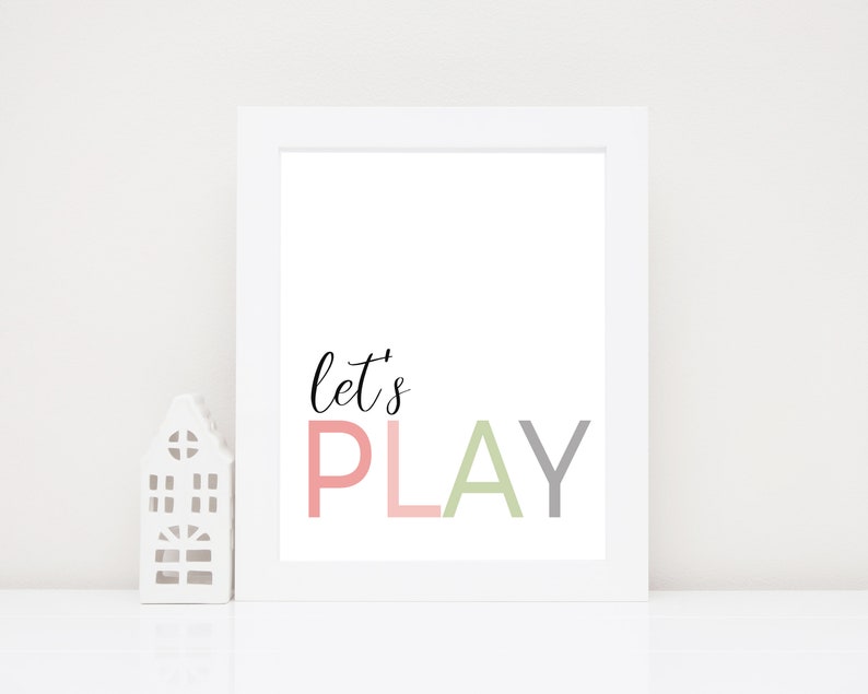 May include: White framed print with the text "let's PLAY" in pink, green, and gray letters. The letters are stacked on top of each other.