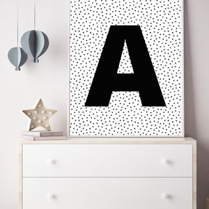 May include: A framed black and white print featuring a large black letter "A" against a background of small black triangles. The artwork is displayed on a white dresser with decorative items, including a star-shaped light and paper hot air balloons.