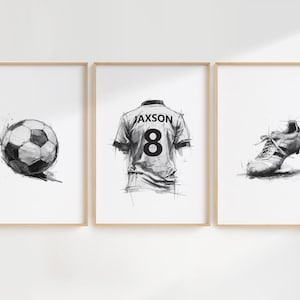 Puede incluir: Tres bocetos en blanco y negro enmarcados. El marco de la izquierda presenta un balón de fútbol, el marco central muestra una camiseta con el nombre "Jaxson" y el número "8", y el marco de la derecha muestra una bota de fútbol.