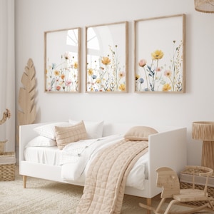 May include: Three framed watercolor prints of floral arrangements with yellow, pink, and blue flowers on a white wall above a white daybed with a beige quilt and pillows.