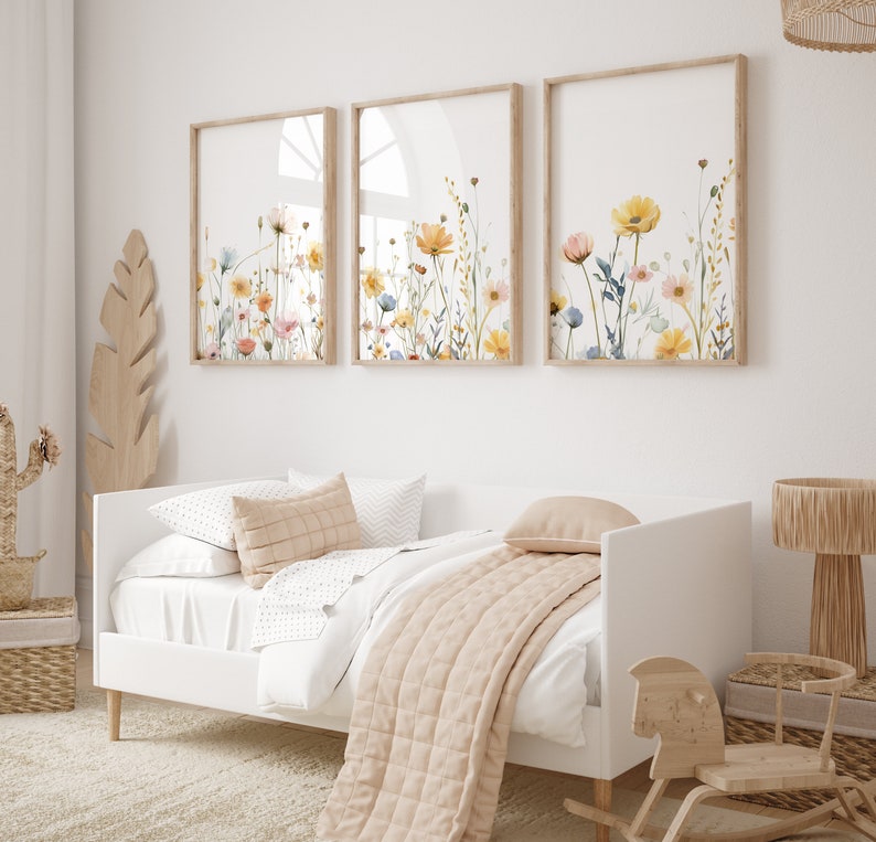 May include: Three framed watercolor prints of floral arrangements with yellow, pink, and blue flowers on a white wall above a white daybed with a beige quilt and pillows.