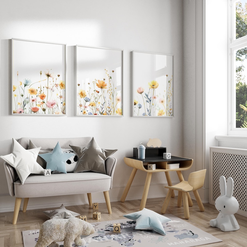 May include: A light gray sofa with three pillows, a wooden desk with a black top, a wooden chair, and a white bunny lamp. The wall behind the sofa has three framed prints of watercolor floral arrangements.