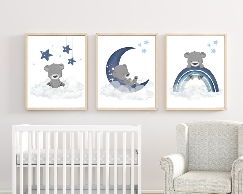 Op de afbeelding: Drie ingelijste prints met een blauw en grijs kleurenschema met een schattige grijze beer op een wolk met sterren, een grijze beer op een halve maan met sterren en een grijze beer op een regenboog met sterren.