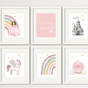 May include: Set of six printable wall art prints featuring a pink and gold color scheme. The prints include a princess with a rainbow, a unicorn, a castle, a carriage, a rainbow, and the text "Dream Big Little One".