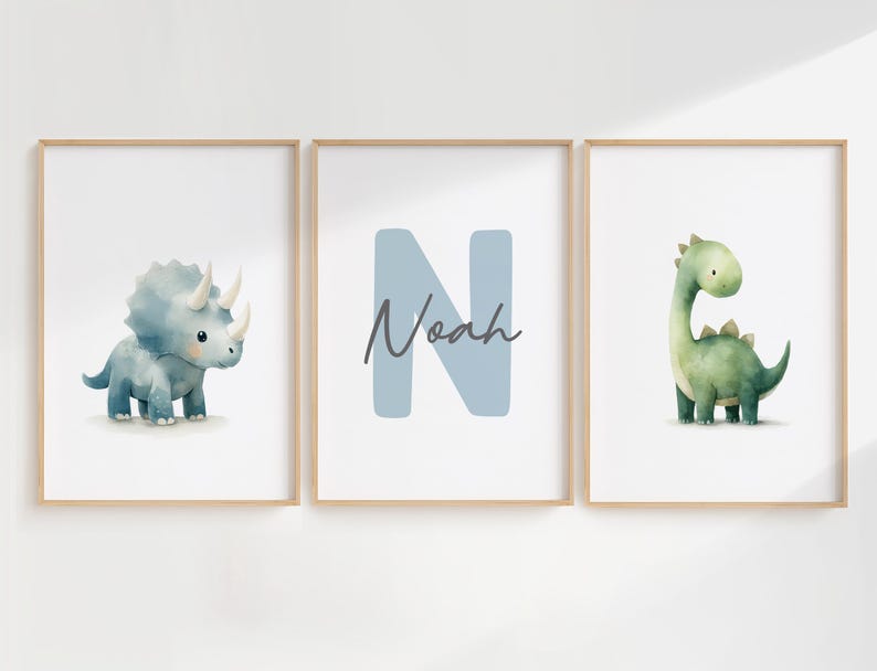 Może przedstawiać: Trzy oprawione wydruki akwarelowe z dinozaurami. Jeden przedstawia niebieskiego triceratopsa, drugi literę "N" z imieniem "Noah", a trzeci zielonego Brontozaura. Wszystkie na białym tle.