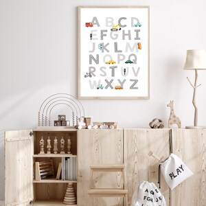 Puede incluir: Un cuadro enmarcado con el alfabeto con veh&iacute;culos coloridos y fondo gris. Las letras son en blanco y negro con un dise&ntilde;o de carretera gris. El cuadro est&aacute; colgado en una pared blanca en una habitaci&oacute;n de ni&ntilde;os.