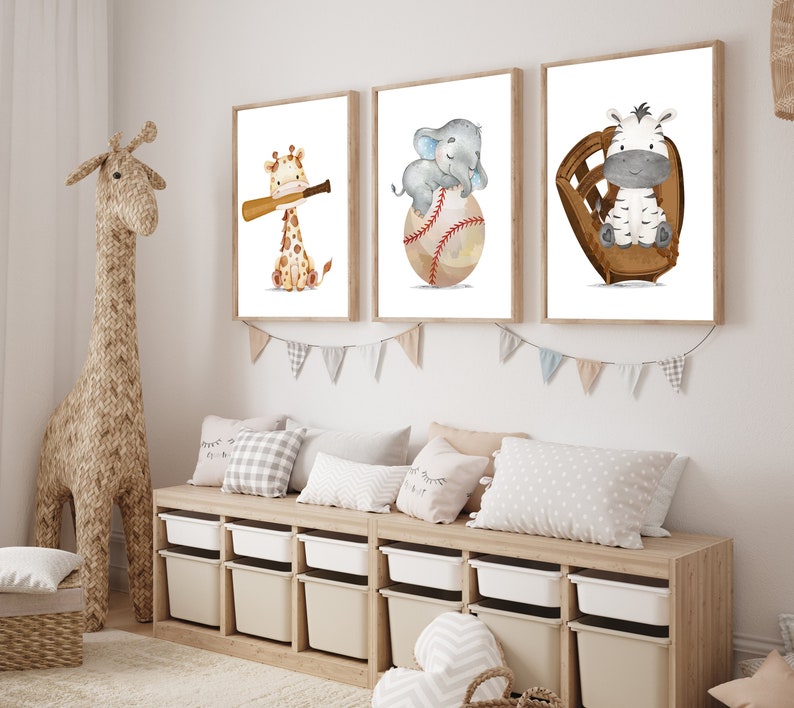K&ouml;nnte beinhalten: Drei gerahmte Drucke mit Aquarell-Illustrationen von Tieren, die Baseball spielen. Die Drucke zeigen eine Giraffe, einen Elefanten und ein Zebra. Die Drucke h&auml;ngen an einer wei&szlig;en Wand &uuml;ber einem Holzregal mit Aufbewahrungskisten.