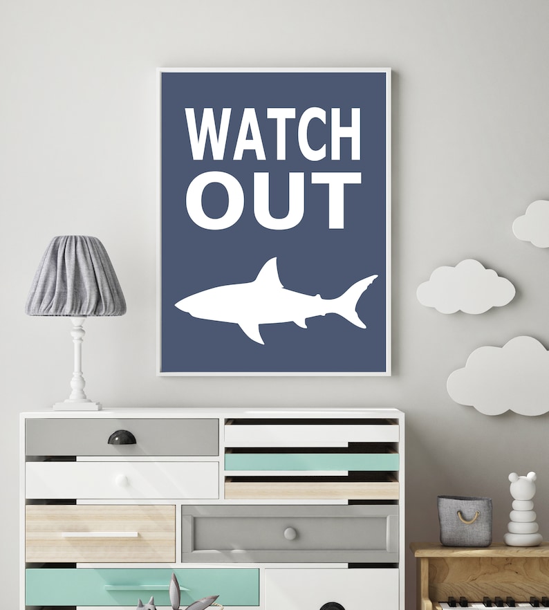 Op de afbeelding: Een blauwe en witte printbare wandkunstprint met de tekst "WATCH OUT" en een wit silhouet van een haai.