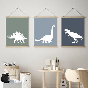 May include: Three framed prints with white dinosaur silhouettes on a light blue, green, and dark blue background. The dinosaurs are a stegosaurus, a brachiosaurus, and a tyrannosaurus rex.