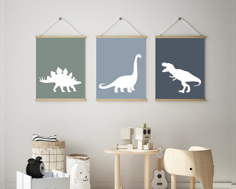 May include: Three framed prints with white dinosaur silhouettes on a light blue, green, and dark blue background. The dinosaurs are a stegosaurus, a brachiosaurus, and a tyrannosaurus rex.