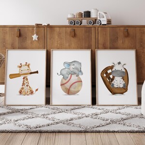 K&ouml;nnte beinhalten: Drei Aquarelldrucke mit einer Giraffe, die einen Baseballschl&auml;ger h&auml;lt, einem Elefanten, der auf einem Baseball sitzt, und einem Zebra, das in einem Baseballhandschuh sitzt. Die Drucke sind gerahmt und auf einem Holzregal ausgestellt.