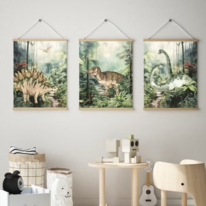 K&ouml;nnte beinhalten: Drei gerahmte Drucke von Dinosauriern in einer Dschungelkulisse. Die Drucke zeigen einen Stegosaurus, einen Tyrannosaurus Rex und einen Brachiosaurus. Die Drucke sind alle im Aquarellstil gehalten und haben ein gr&uuml;n-braunes Farbschema.
