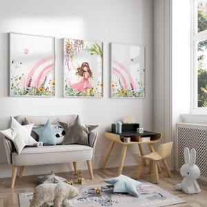 May include: Three watercolor prints featuring a fairy with pink wings and a pink dress standing in a field of flowers with a rainbow in the background. The prints are framed in white and hung on a white wall.